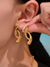 Gold hoop earrings being worn and adjusted by a hand.