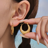 Gold hoop earrings being worn and held up to an ear against a neutral background